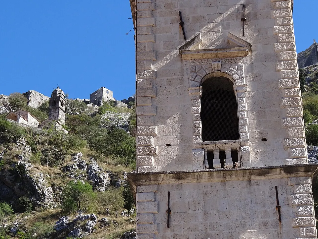 An old stone bell tower in Kotor's Old Town, the steep city walls and fortifications climbing the rocky hillside behind