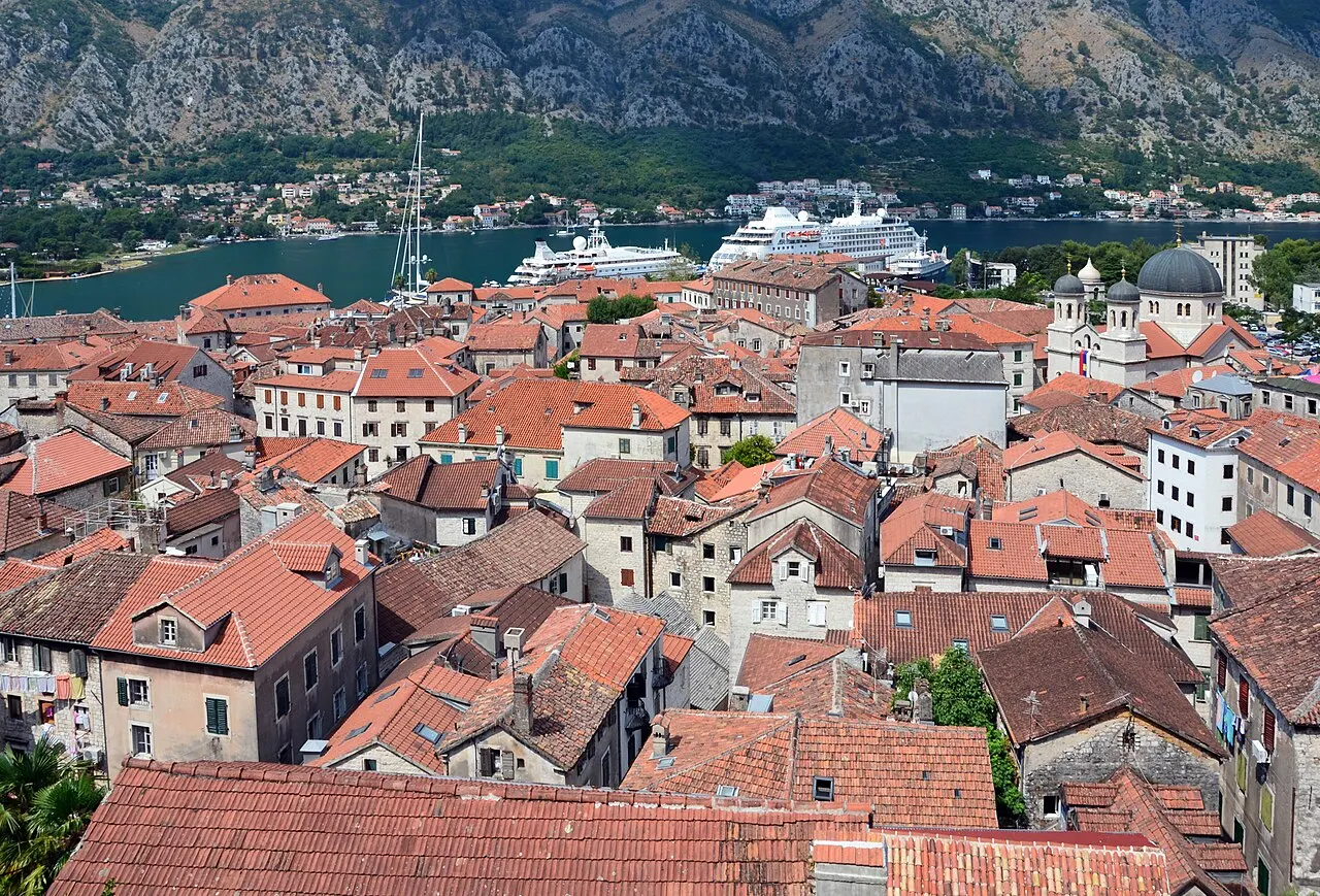 The red-tiled rooftops of Kotor's Old Town with the Bay of Kotor and a cruise ship beyond, the view from the hillside