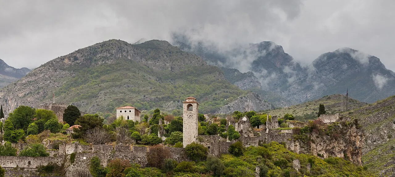 The ruined stone town of Stari Bar with its clock tower and old walls spread on a hill below cloud-draped mountains
