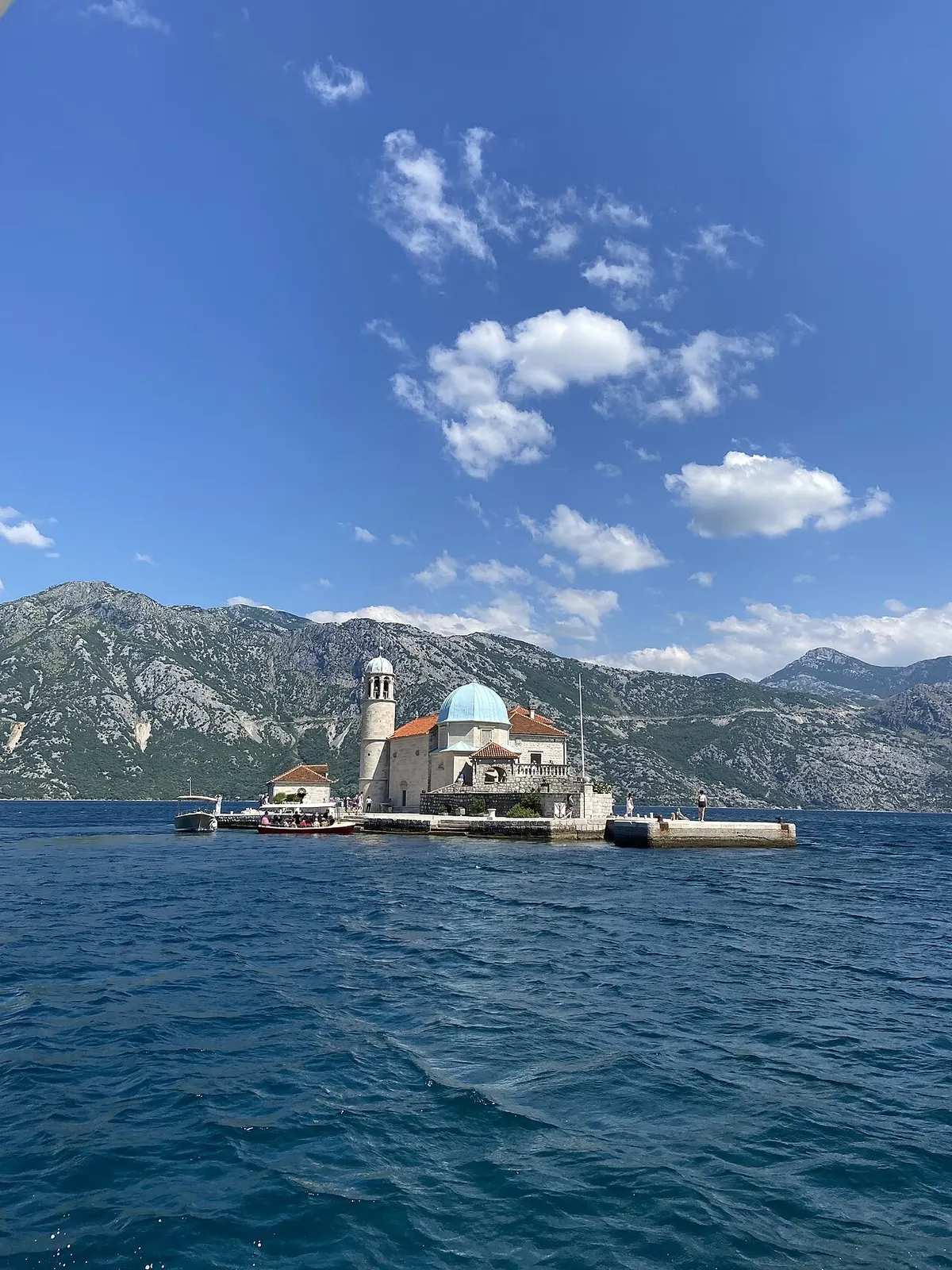 The island church of Our Lady of the Rocks off Perast on the calm Bay of Kotor, a small boat docked beneath the mountains