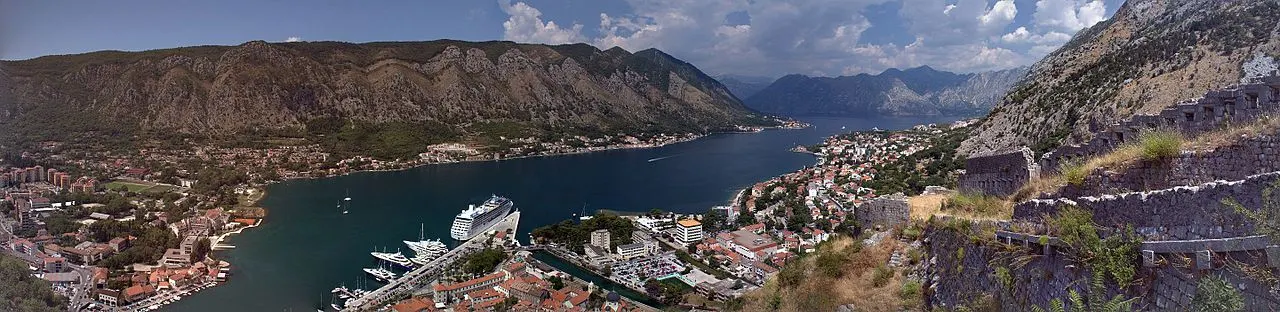 Panorama of Kotor and its bay with boats and a cruise ship on the water and steep mountains rising on every side