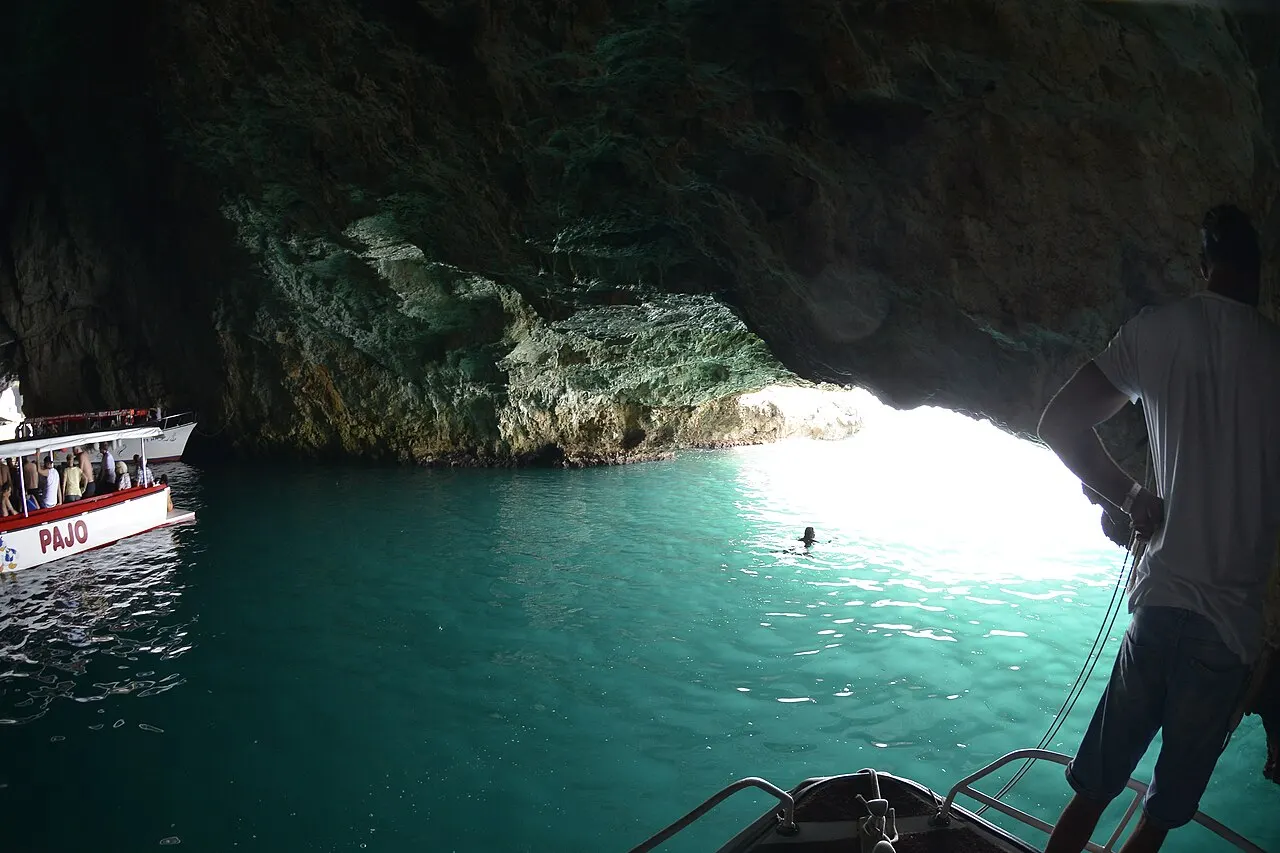 Inside the Blue Cave, water glowing electric turquoise beneath the rock and a tour boat at the bright cave mouth