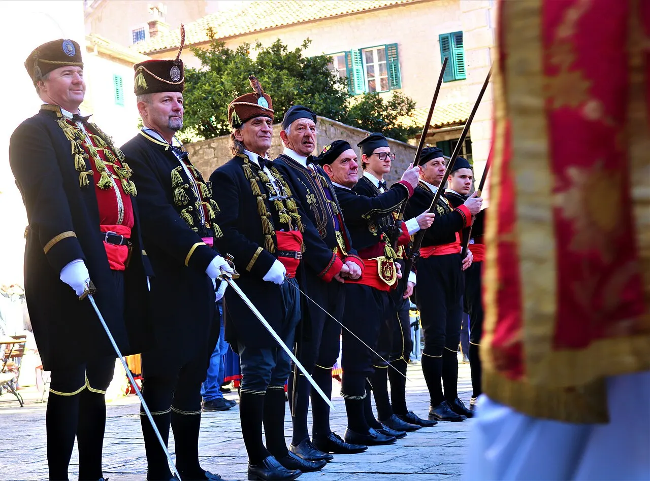 Boka Navy members in formation on a Kotor square holding swords, in detailed black-and-gold braided historic uniforms
