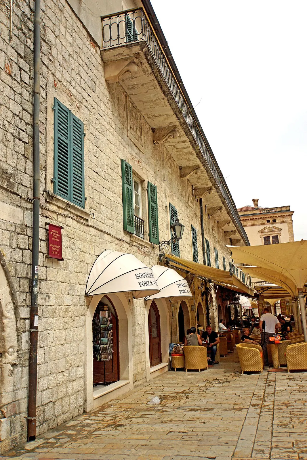 A restored stone Venetian-era palace in Kotor's Old Town with green shutters, arched doorways and a terrace below