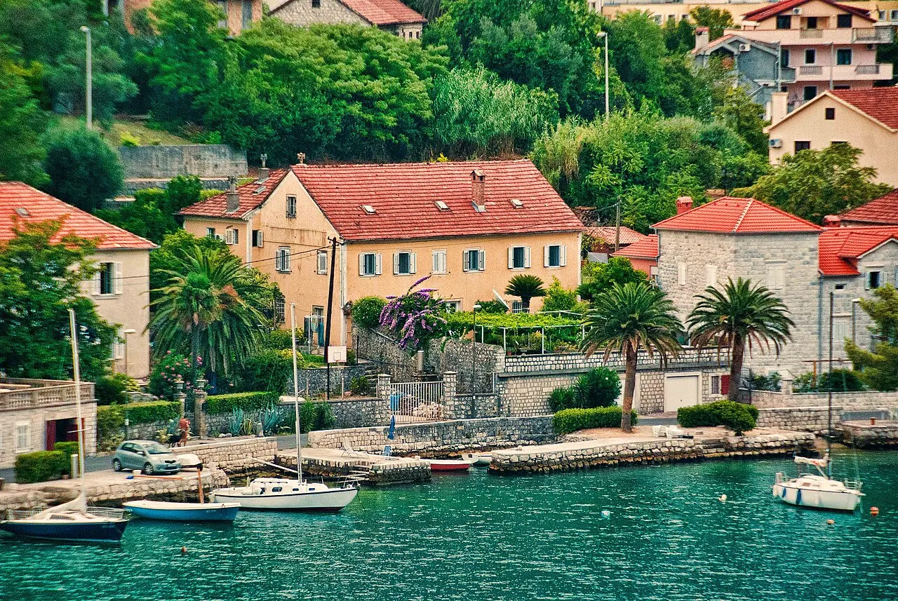 A stone waterfront house with a terraced garden and palms in Dobrota on the Bay of Kotor, boats moored on the calm bay