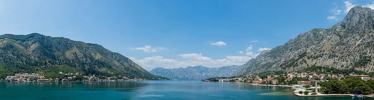 A wide panorama of the Bay of Kotor, calm water ringed by steep mountains with waterside settlements below