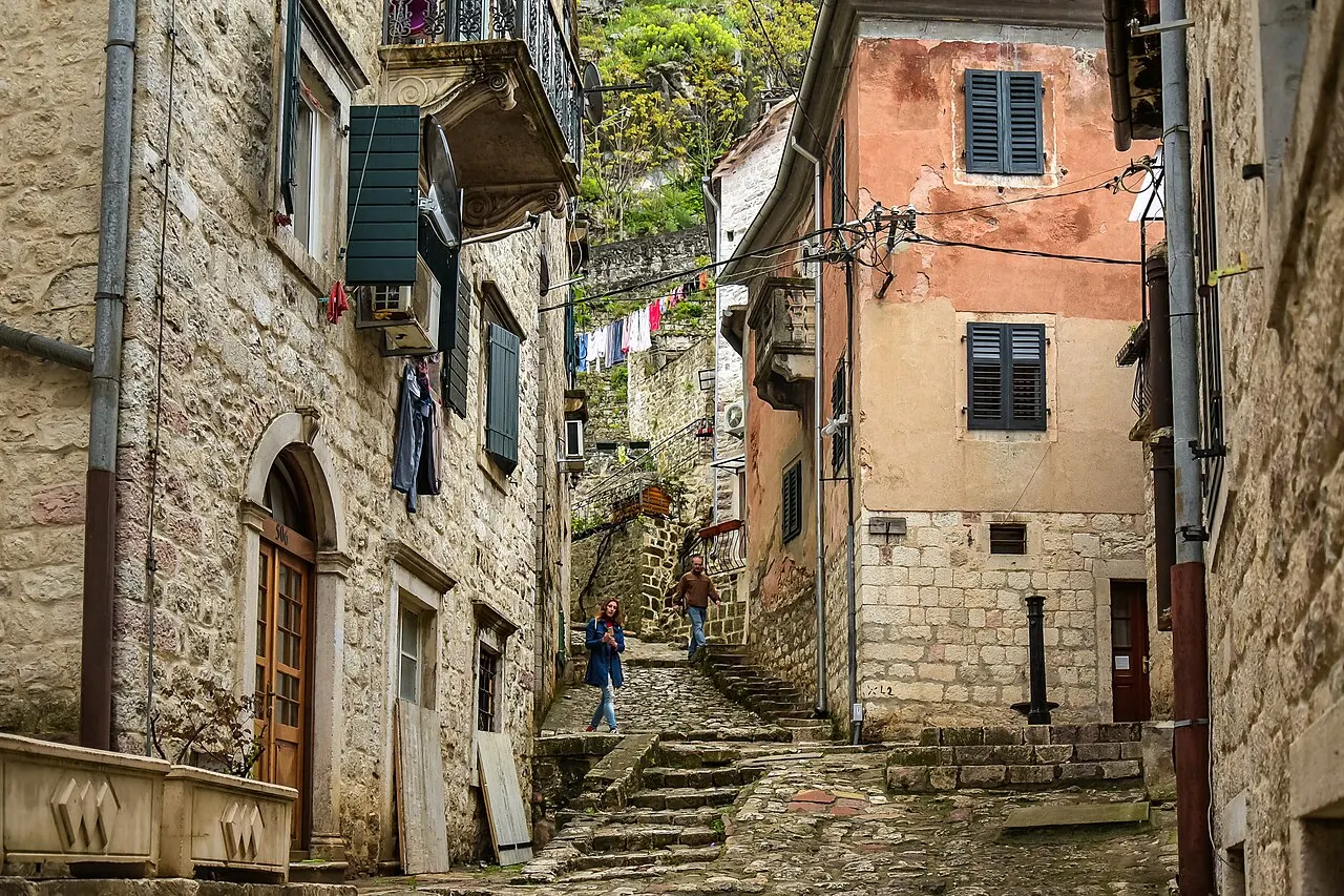 A steep stone stairway climbing between old shuttered houses in Kotor, Montenegro, narrow steps and no lift in sight