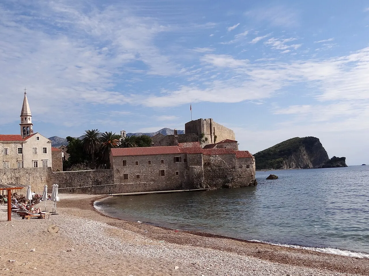 A narrow stone lane in Budva's Stari Grad, weathered facades and shutters opening toward the citadel and sea