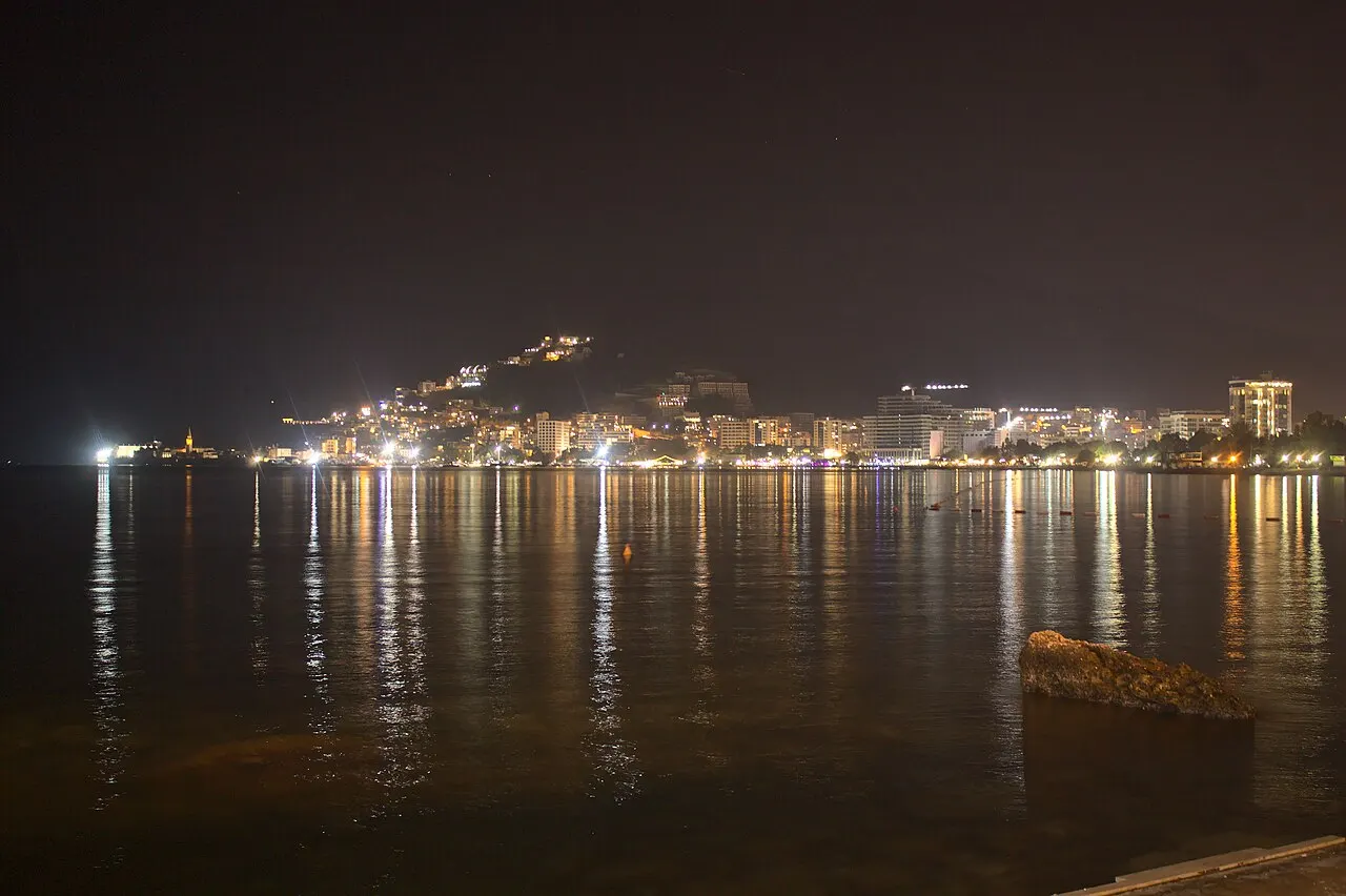 The Budva riviera lit up after dark, the old town and waterfront glowing against the night bay