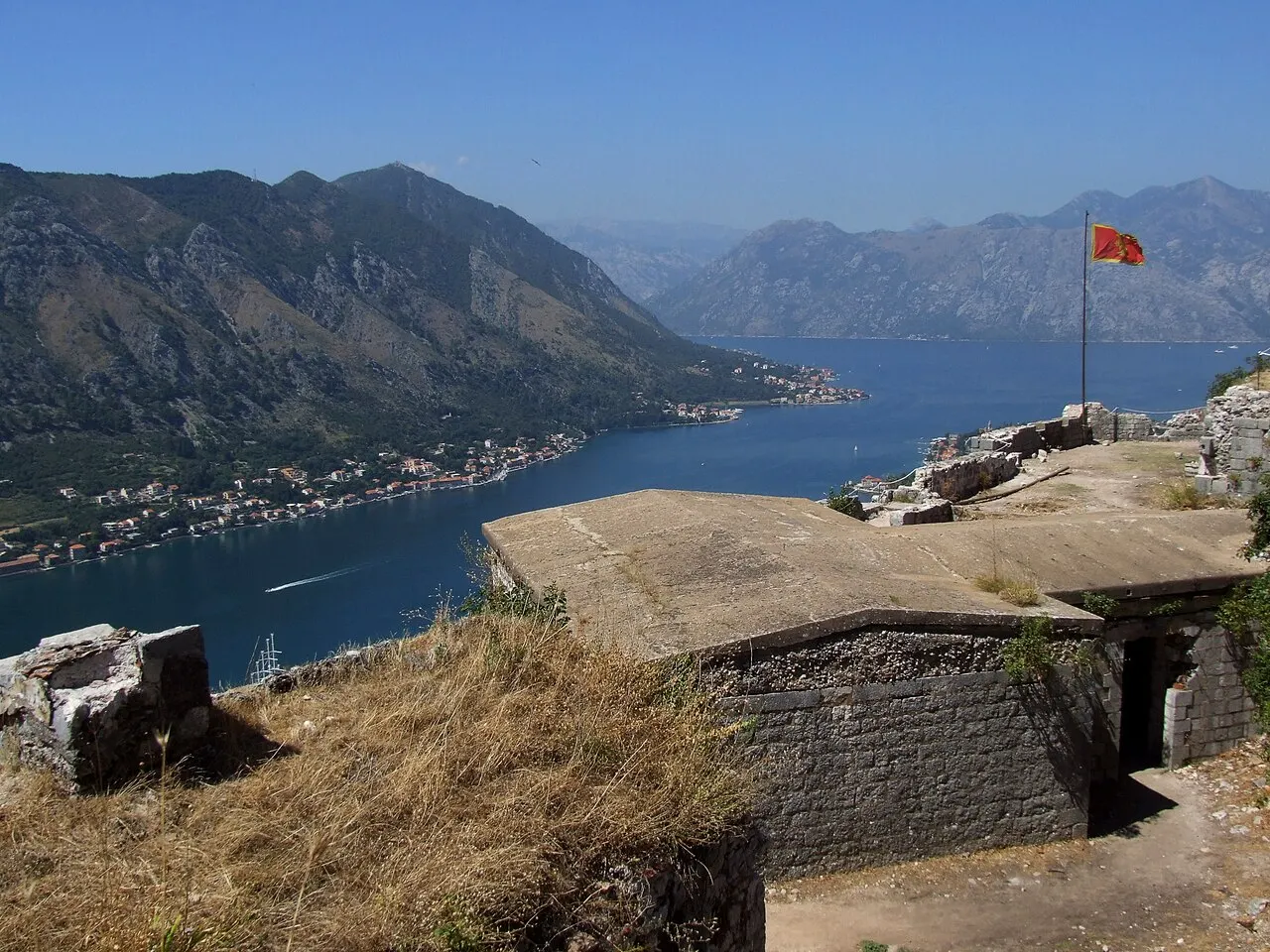 Panorama of the Bay of Kotor from the fortress ramparts, a Montenegrin flag flying above the bastion and bay below