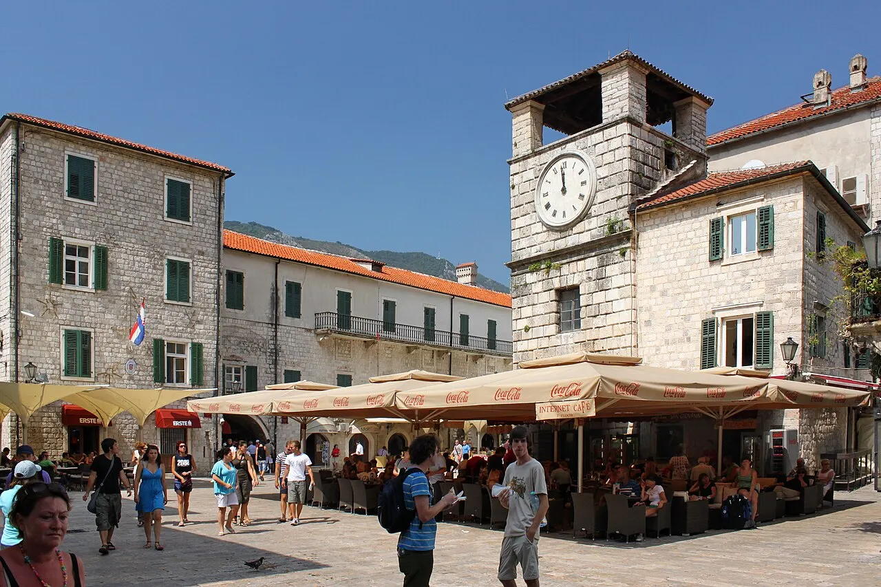 Kotor's Arms Square with the stone Clock Tower, café umbrellas and tables spread across the flagstones and visitors strolling