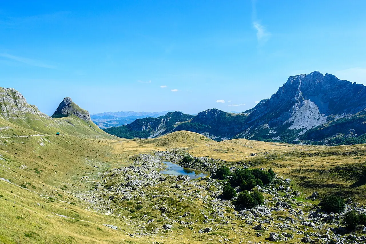 Limestone peaks of Durmitor rising above grassland and a small glacial pond in the wild interior of Montenegro