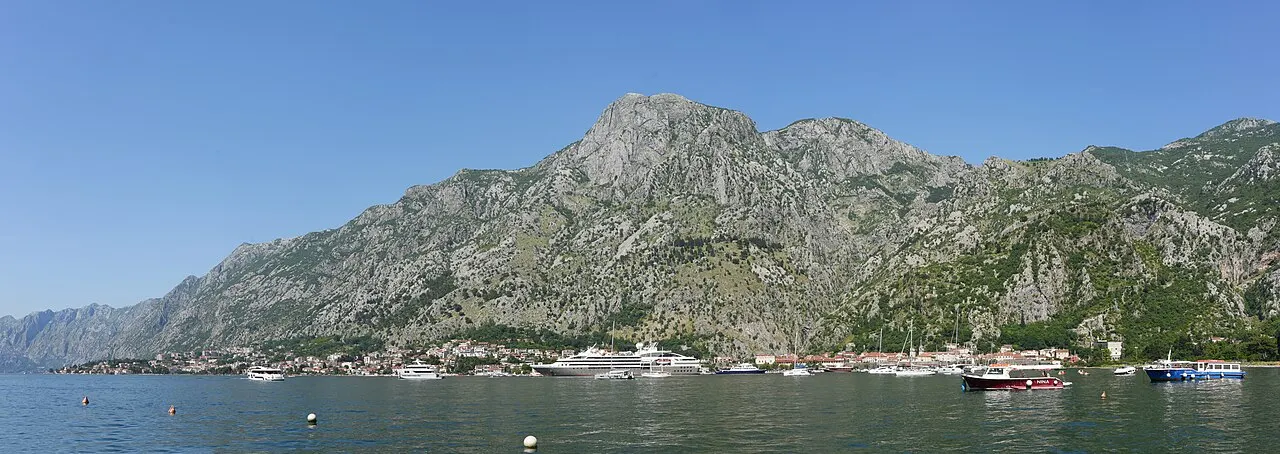 A quiet stretch of the Bay of Kotor at Muo, boats on the water and steep limestone mountains behind