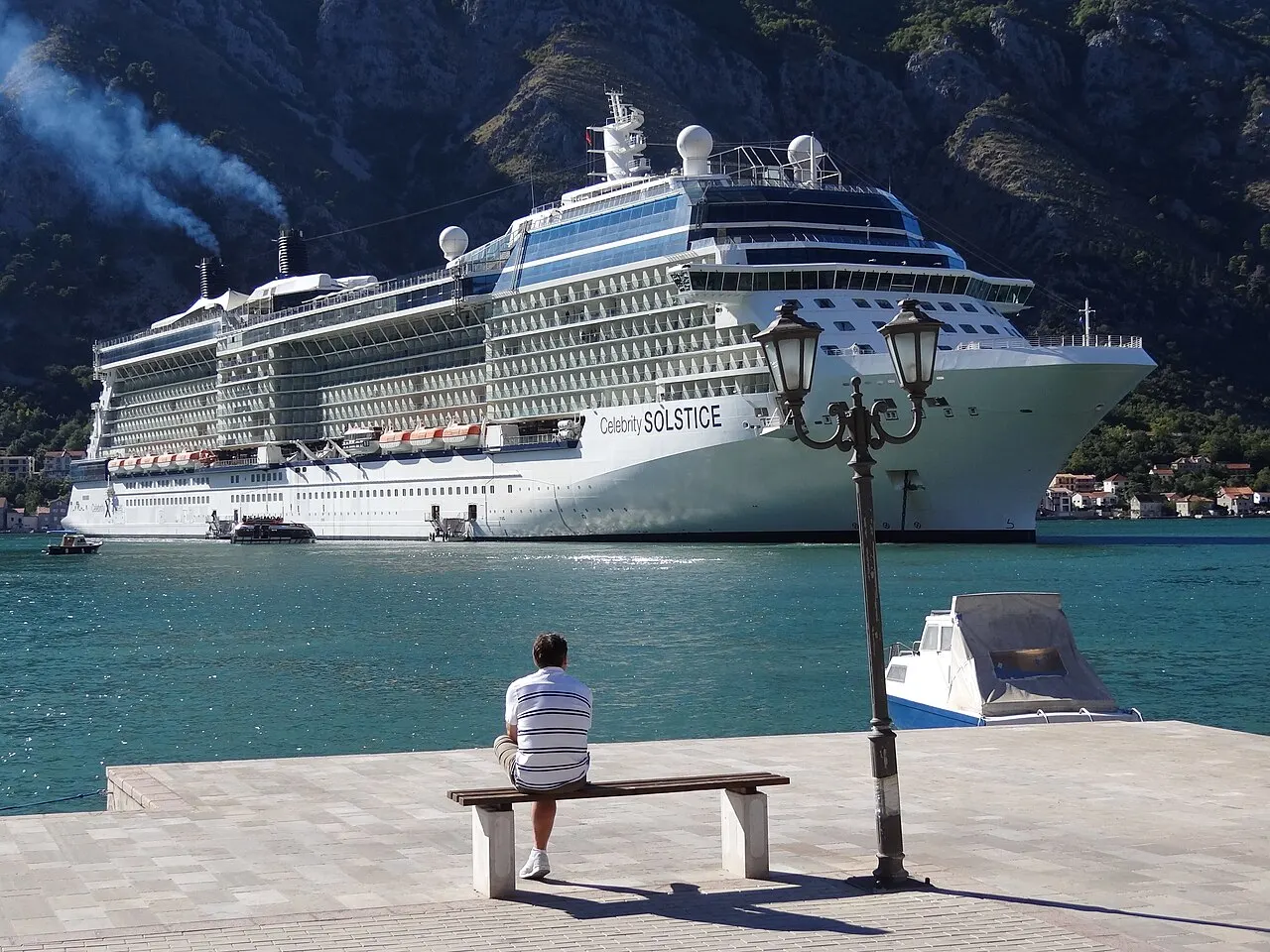 A large cruise ship moored at the Kotor quay just outside the Old Town, mountains rising behind