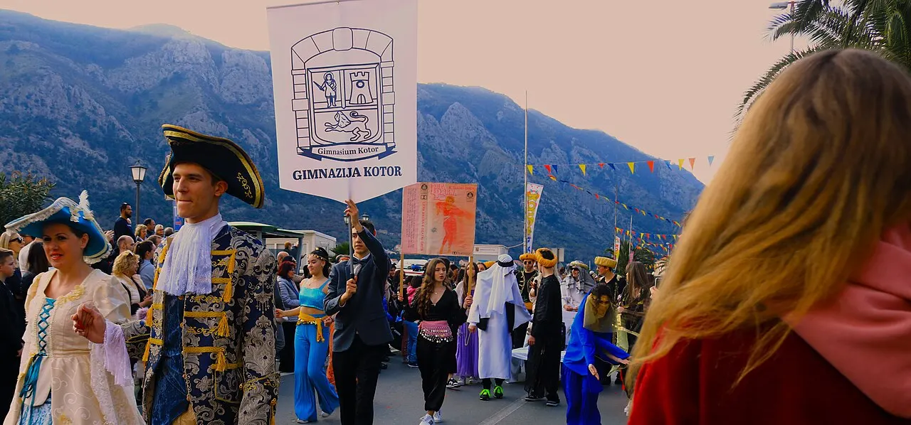 Costumed revellers parading at the Kotor Carnival, mountains rising behind