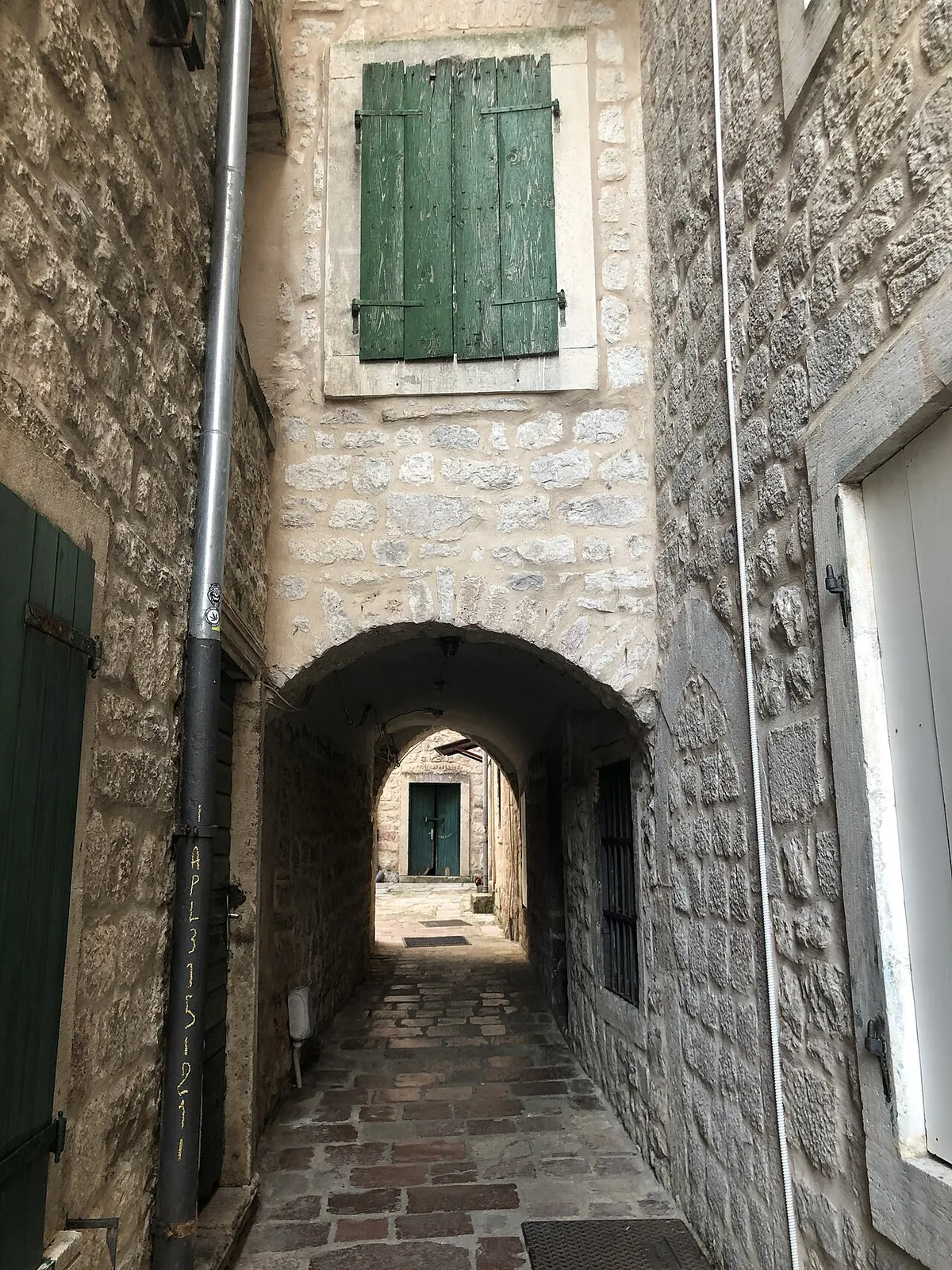 A narrow cobbled stone lane with an arch and green shutters inside Kotor Old Town