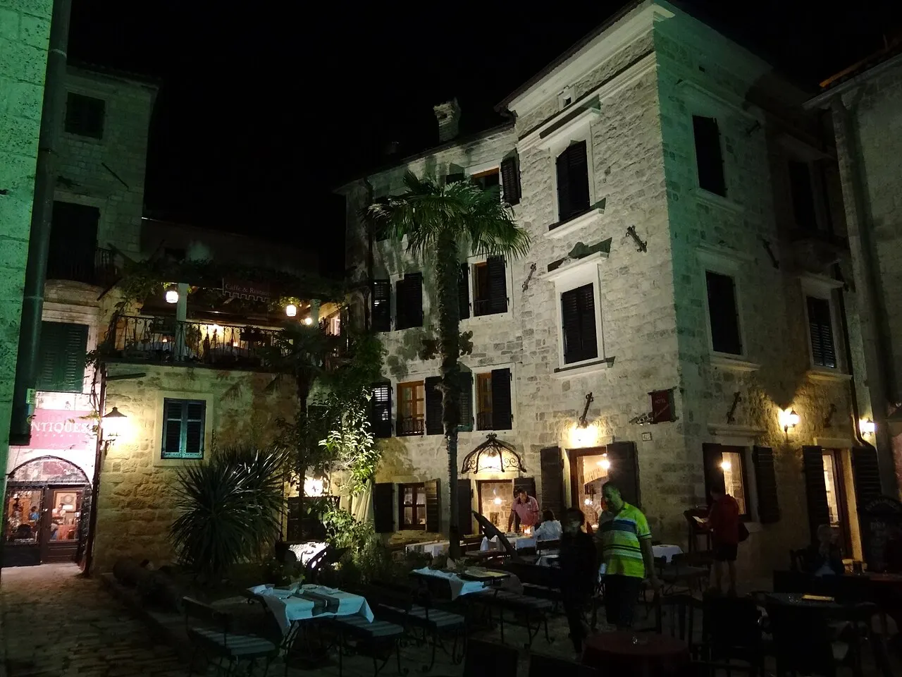 A konoba with restaurant tables tucked into a stone-walled corner of Kotor Old Town at night