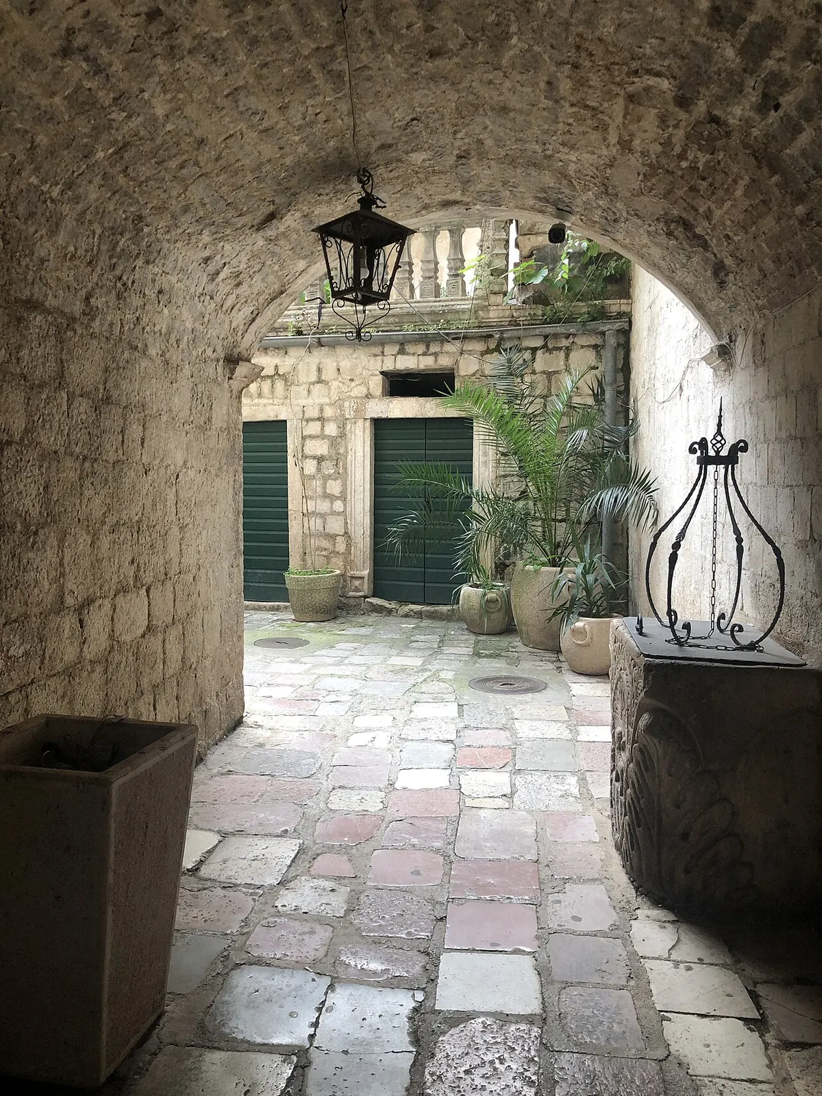 A quiet lamplit stone square in Kotor Old Town at night with a fountain and cats