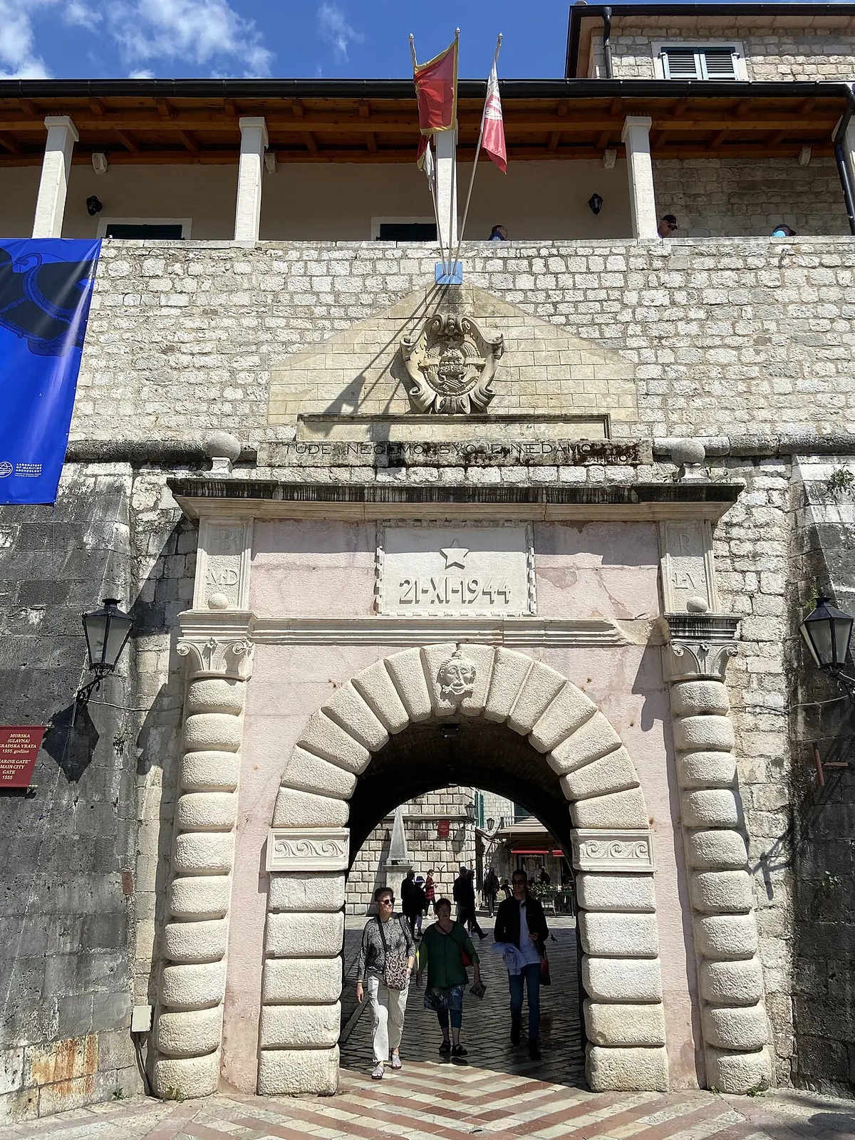 People passing through the Sea Gate into Kotor's Old Town, the walls rising above