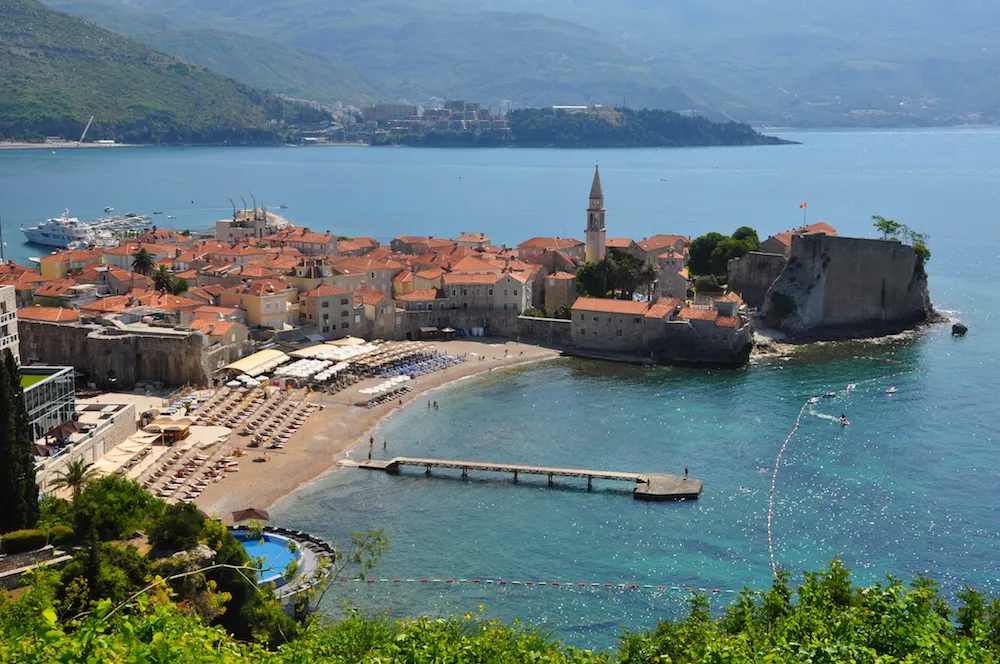 Budva's walled old town above its city beach with sunbeds and clear Adriatic water