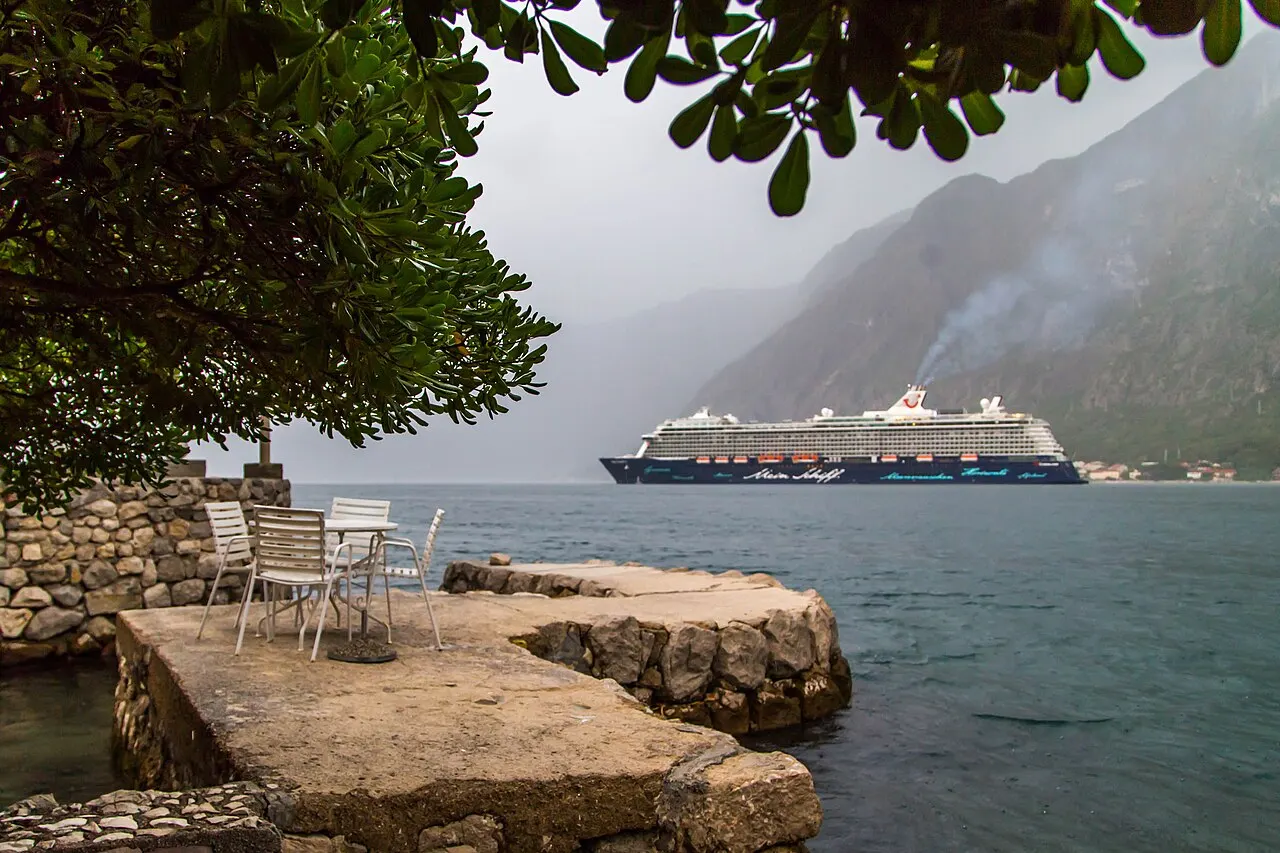 Waterfront terrace with a cafe table by the water at Prcanj, a cruise ship and the Bay of Kotor beyond