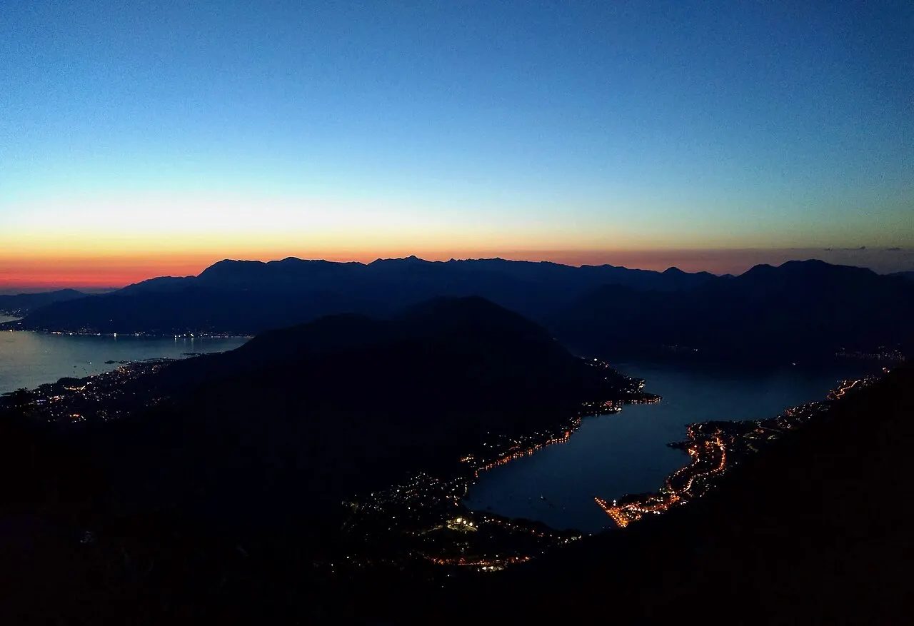 The Bay of Kotor at dusk seen from the lookout above, town lights glowing along the water