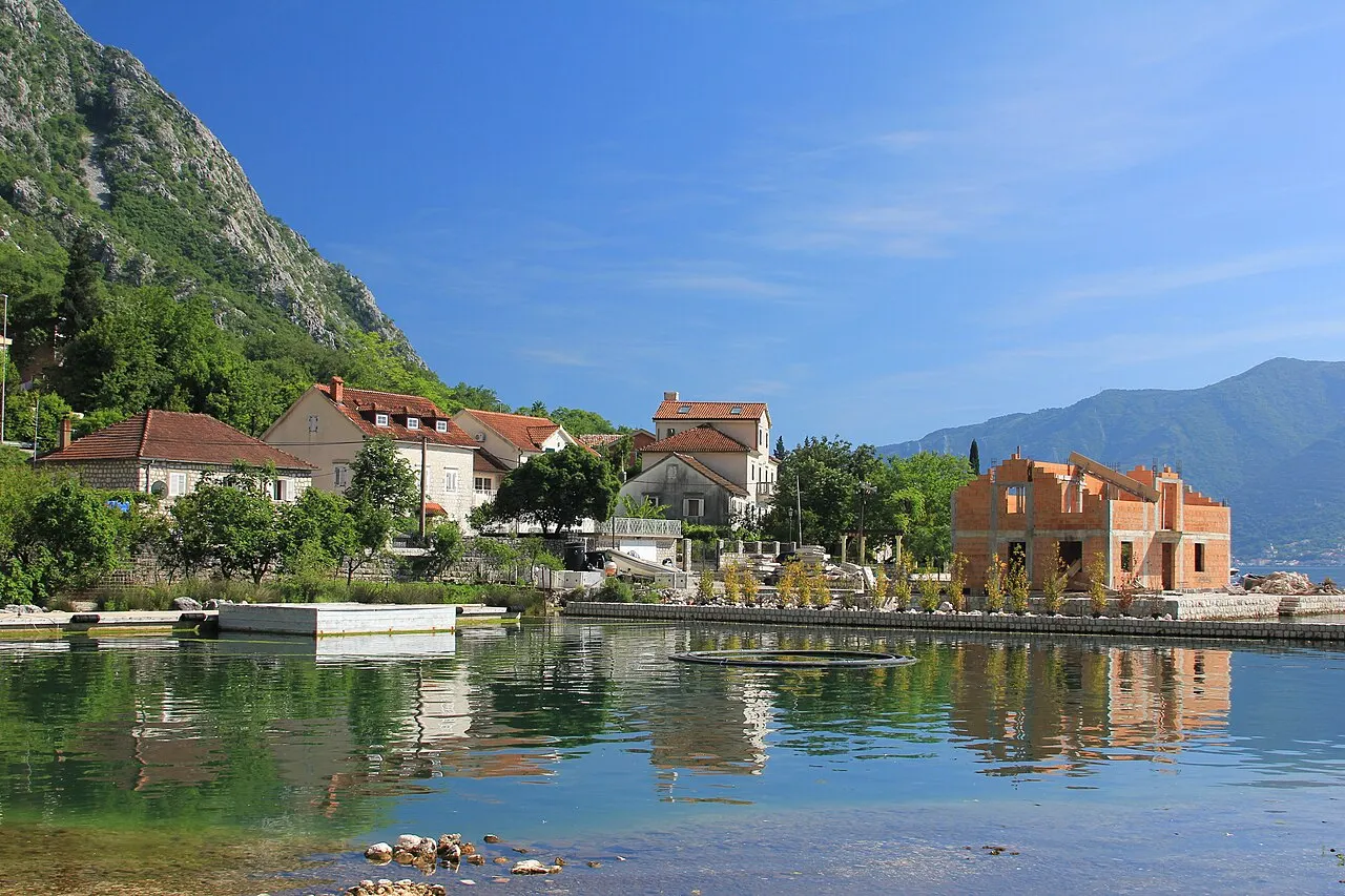 Orahovac village strung along the Bay of Kotor shore, clear water and beach platforms below steep mountains