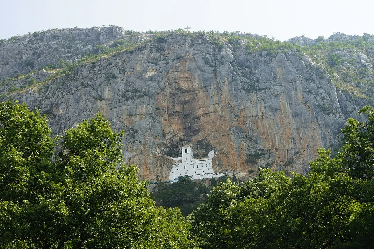 The white Upper Monastery of Ostrog set into the grey cliff face, framed by green trees below