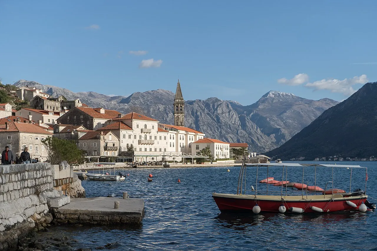 The curved Perast waterfront of stone palaces and the St Nicholas bell tower on the still bay