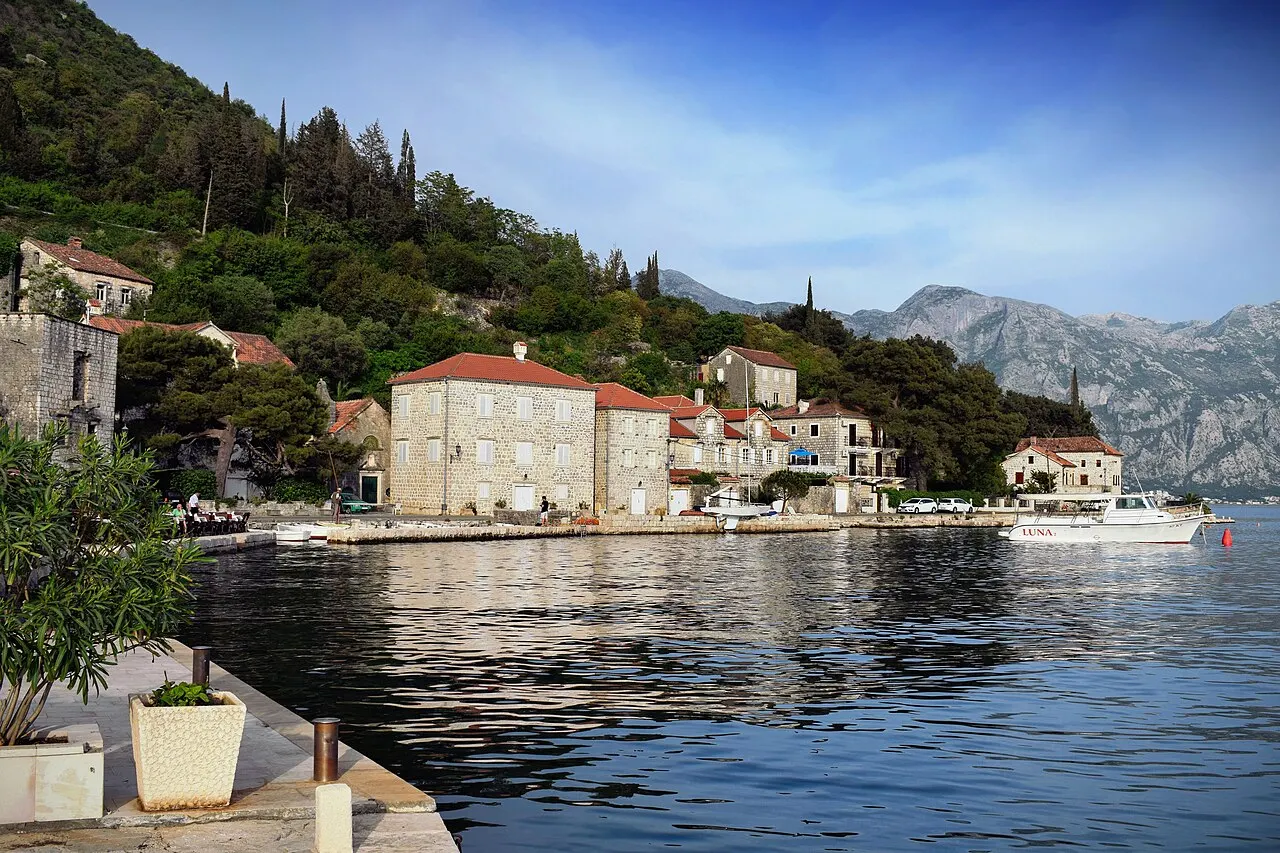 The Perast waterfront and quay edge in warm afternoon light, boats on the calm bay