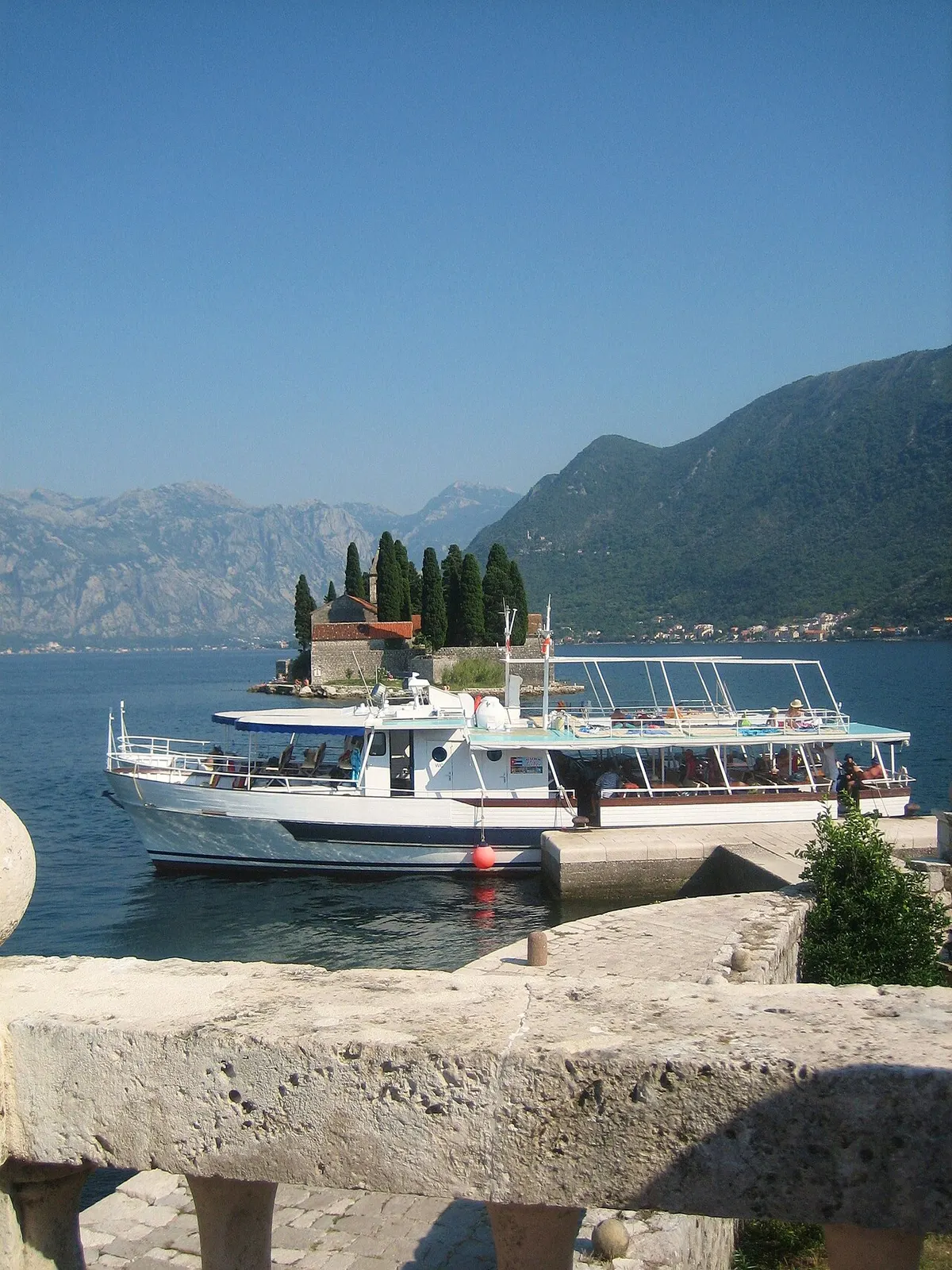 A small boat on the glassy inner Bay of Kotor near Sveti Đorđe islet, mountains rising behind
