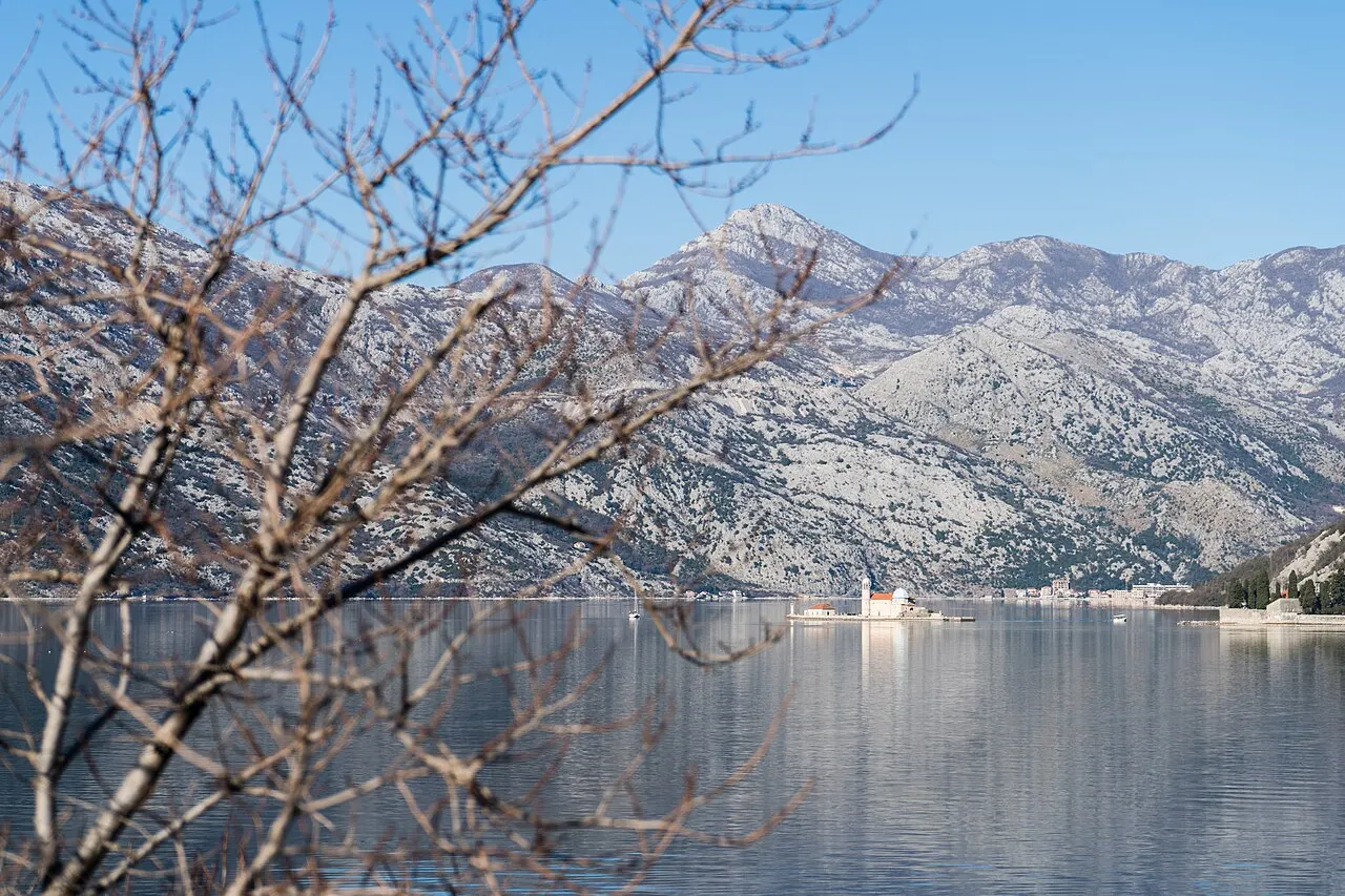 Our Lady of the Rocks island and Perast under low grey cloud on the flat-calm bay