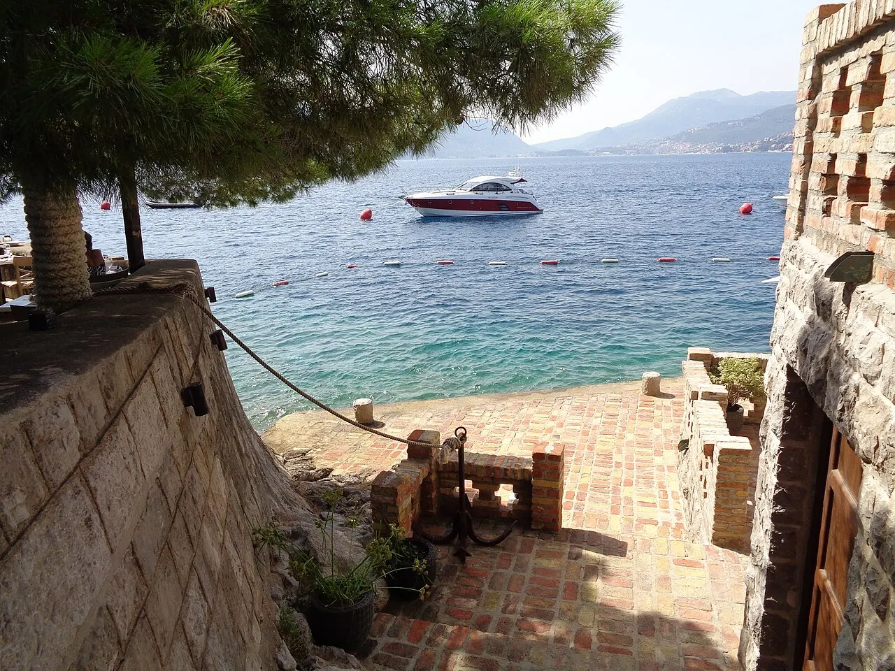 Clear deep water off the rocks at Rose, a boat moored and the Bay of Kotor opening beyond