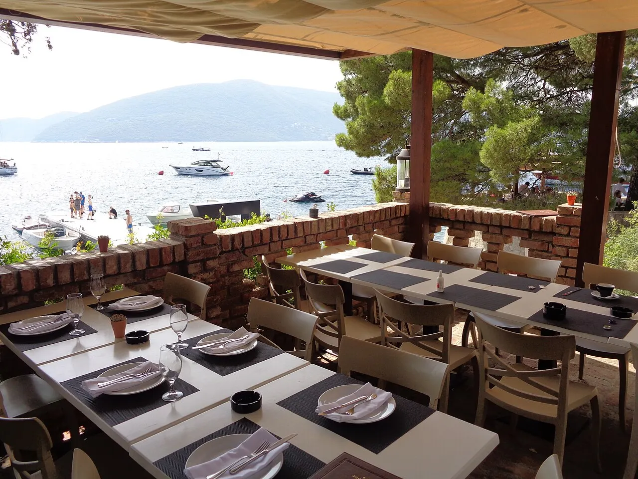 A waterfront konoba terrace at Rose with tables set, boats and the bay just beyond the edge