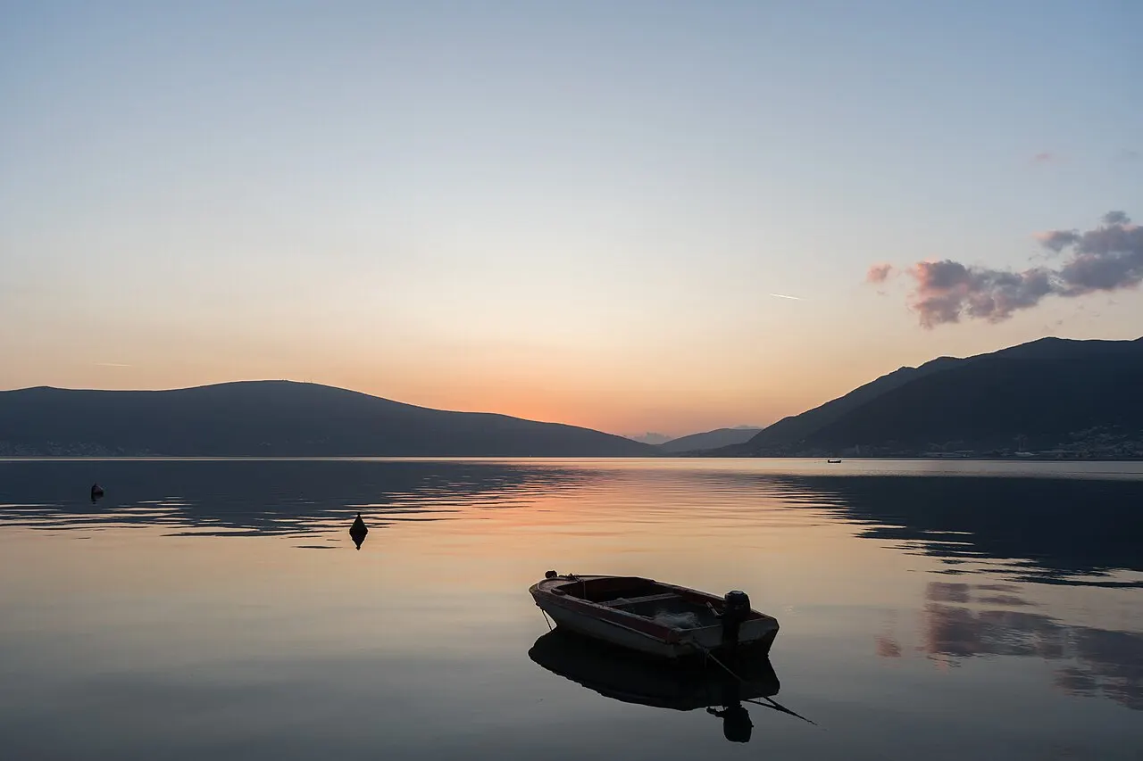 A small boat on the glassy inner Bay of Kotor at sunset, mountains darkening around the still water
