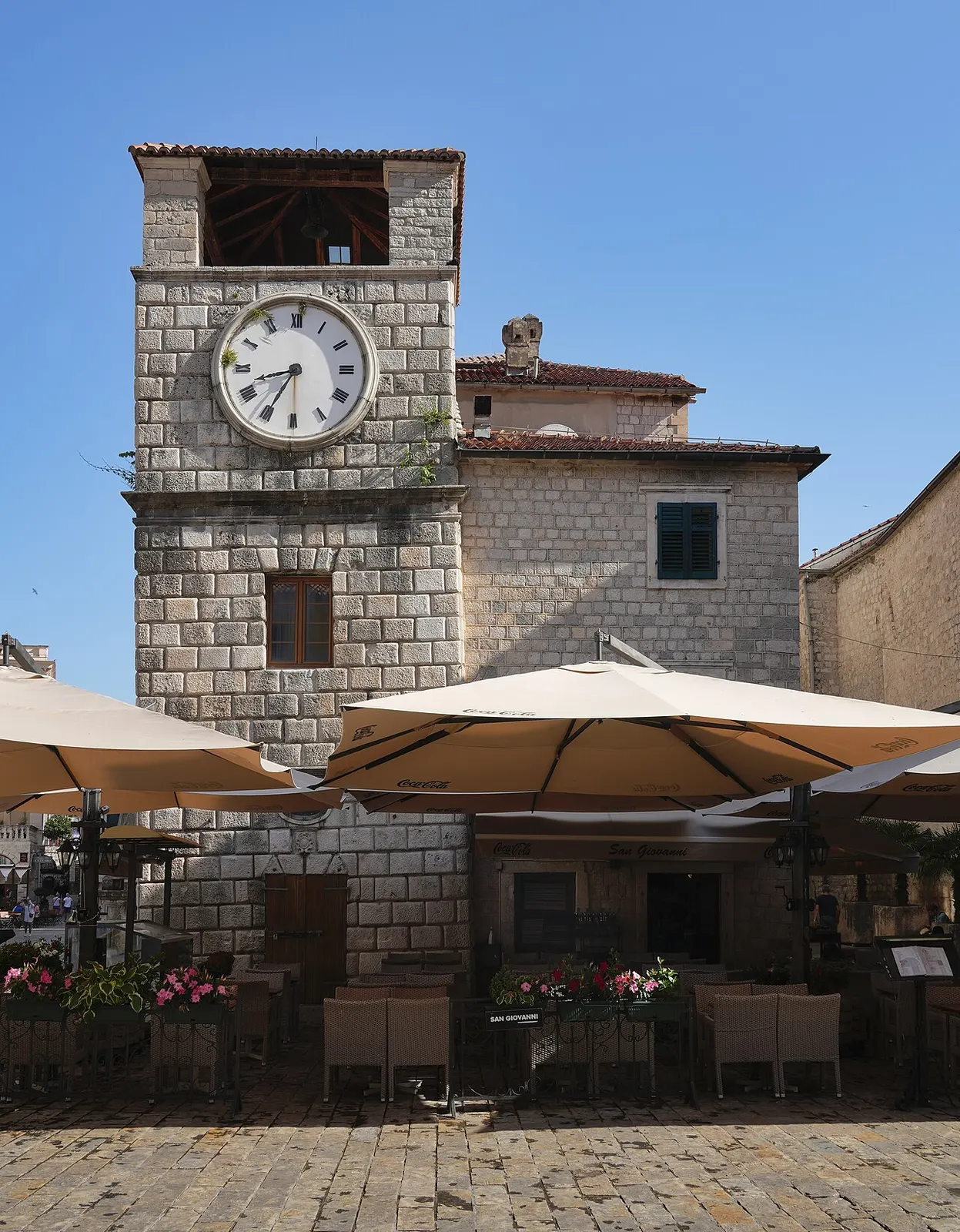 Café terraces and umbrellas below the stone Clock Tower on Arms Square, just inside the Sea Gate