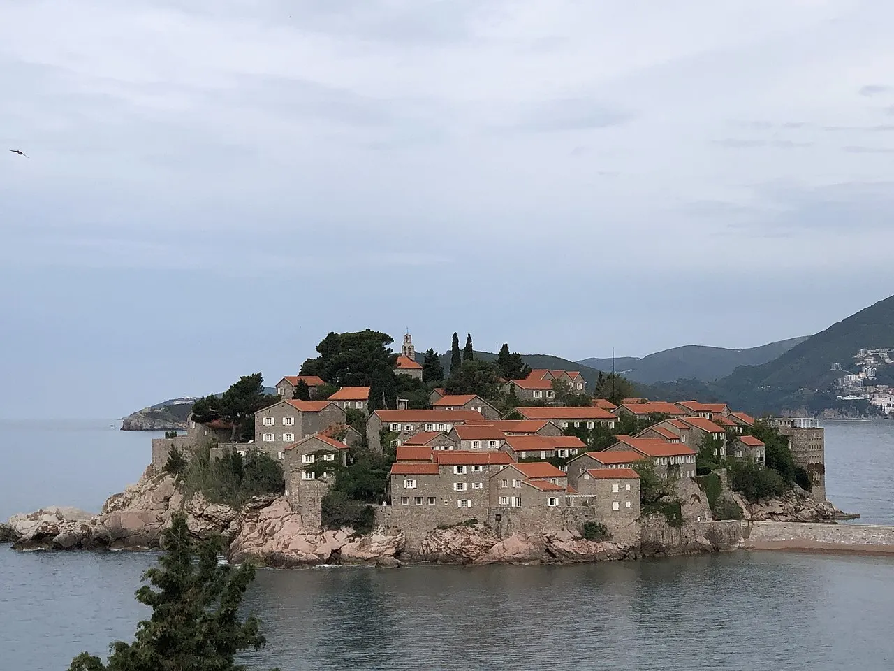 The islet of Sveti Stefan with terracotta roofs and its sandy causeway against the Adriatic