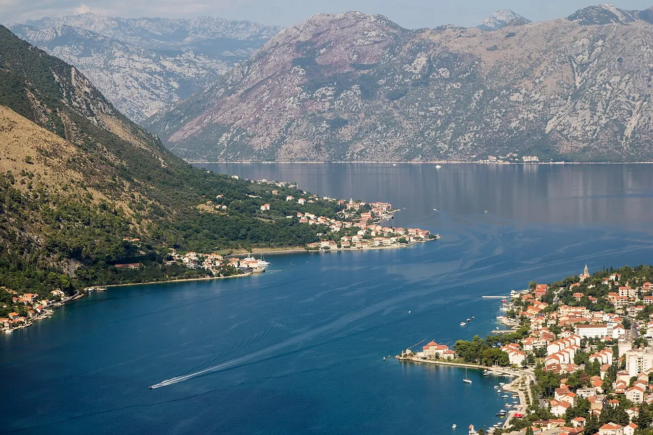 High view from St John castle over the inner Bay of Kotor, terracotta-roofed shore towns and a boat on the water